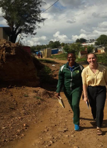 two smiling young woman walk side by side on a winding dirt road